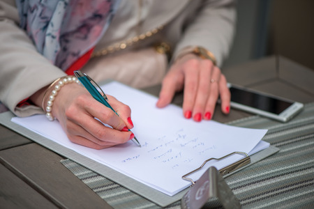 Close-up of female hands. Woman writing something sitting at cafe. Signing documents.の写真素材