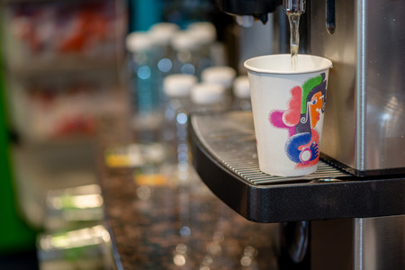 Selective focus close up of the coffee machine fills the hot water in a colored paper cup.の写真素材