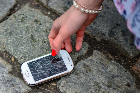 Person Picking Broken Smart Phone (Cracked Screen) of the Groundの写真素材