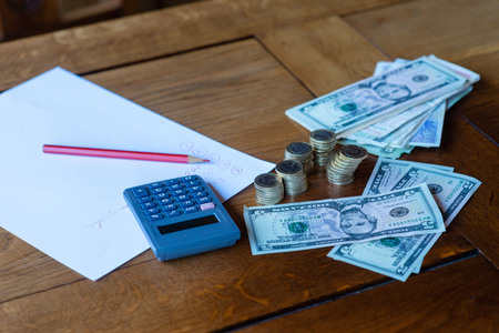 Close up man with calculator counting, making notes at home, hand is writes in a notebook. Stacked coins arranged at deesk. Savings finances concept.の写真素材