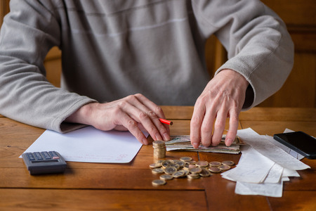 Close up man with calculator counting, making notes at home, hand is writes in a notebook. Stacked coins arranged at deesk. Savings finances concept.の写真素材