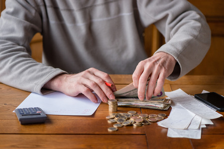 Close up man with calculator counting, making notes at home, hand is writes in a notebook. Stacked coins arranged at deesk. Savings finances concept.の写真素材