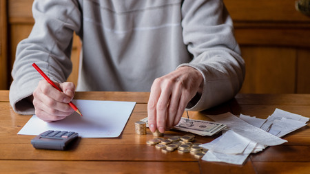 Close up man with calculator counting, making notes at home, hand is writes in a notebook. Stacked coins arranged at deesk. Savings finances concept.の写真素材