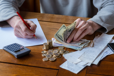 Close up man with calculator counting, making notes at home, hand is writes in a notebook. Stacked coins arranged at deesk. Savings finances concept.の写真素材