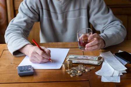 Close up man with calculator counting, making notes at home, hand is writes in a notebook. Stacked coins arranged at deesk. Savings finances concept.の写真素材