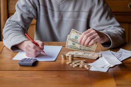 Close up man with calculator counting, making notes at home, hand is writes in a notebook. Stacked coins arranged at deesk. Savings finances concept.の写真素材