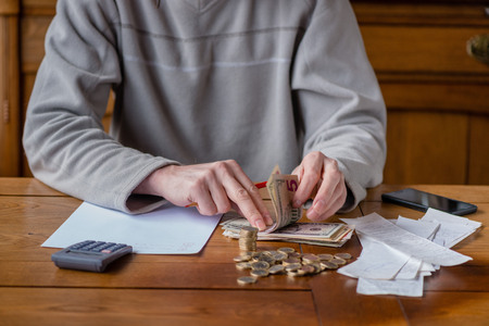 Close up man with calculator counting, making notes at home, hand is writes in a notebook. Stacked coins arranged at deesk. Savings finances concept.の写真素材