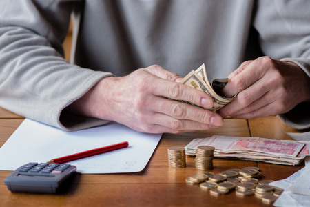 Close up man with calculator counting, making notes at home, hand is writes in a notebook. Stacked coins arranged at deesk. Savings finances concept.の写真素材