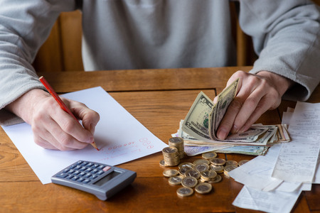 Close up man with calculator counting, making notes at home, hand is writes in a notebook. Stacked coins arranged at deesk. Savings finances concept.の写真素材