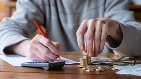 Close up man with calculator counting, making notes at home, hand is writes in a notebook. Stacked coins arranged at deesk. Savings finances concept.の写真素材
