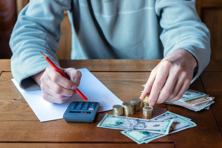 Close up man with calculator counting, making notes at home, hand is writes in a notebook. Stacked coins arranged at deesk. Savings finances concept.の写真素材