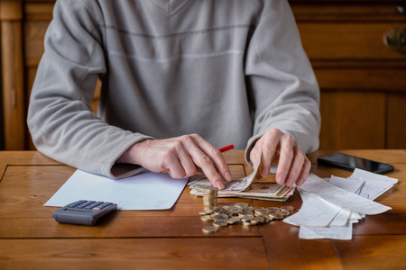 Close up man with calculator counting, making notes at home, hand is writes in a notebook. Stacked coins arranged at deesk. Savings finances concept.の写真素材