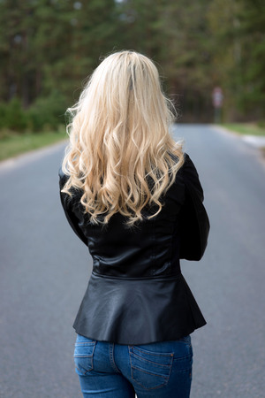 Woman from behind. A young blond woman goes through the asphalt road.の写真素材