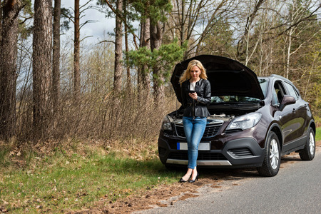 young attractive desperate and confused woman stranded on roadside with broken car engine failure crash accident calling on mobile phone for mechanic assistance in insurance company conceptの写真素材