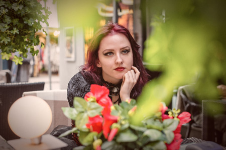 Young gorgeous redheaded woman sitting in an outdoor cafe dressed in retro fashion clothes.の写真素材