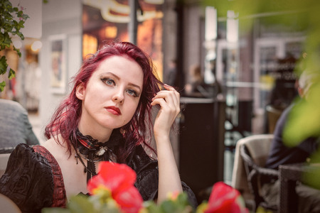Young gorgeous redheaded woman sitting in an outdoor cafe dressed in retro fashion clothes.の写真素材