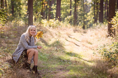 A young, blonde woman walking through the forest on a sunny autumn day.の写真素材