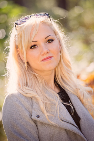 A young, blonde and smiling woman portrait on a sunny autumn day.の写真素材
