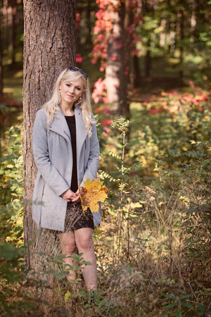 A young, blonde woman walking through the forest on a sunny autumn day.の写真素材