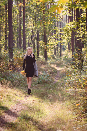 A young, blonde woman walking through the forest on a sunny autumn day.の写真素材