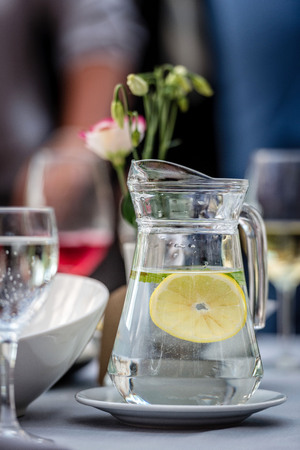 Table laying concept. On the table stands a jug with water and lemon. Glasses in the background.の写真素材