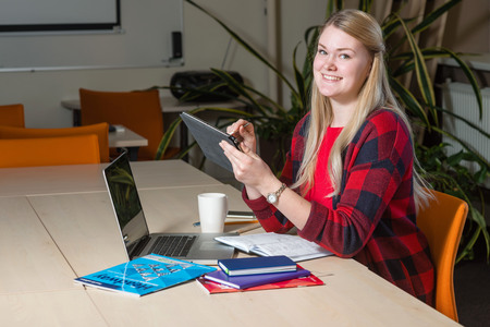 Smiling blonde woman sitting at a laptop drinking tea and working.の写真素材