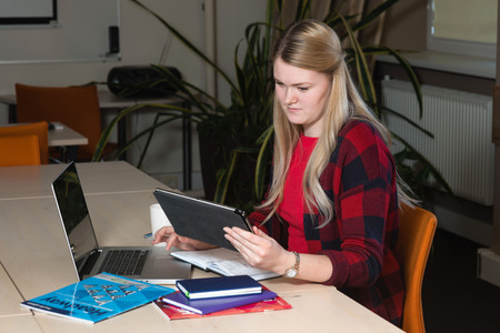 Smiling blonde woman sitting at a laptop drinking tea and working.の写真素材