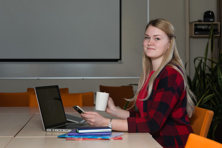 Smiling blonde woman sitting at a laptop drinking tea and working.の写真素材