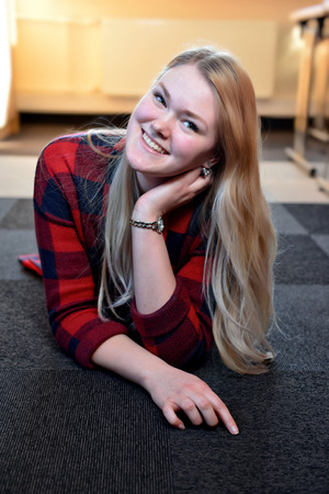 A smiling blonde woman in a red checkered shirt lying on the floor.の写真素材