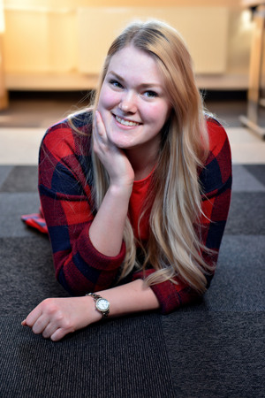 A smiling blonde woman in a red checkered shirt lying on the floor.の写真素材