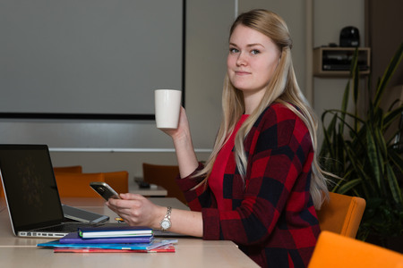 Smiling blonde woman sitting at a laptop drinking tea and working.の写真素材