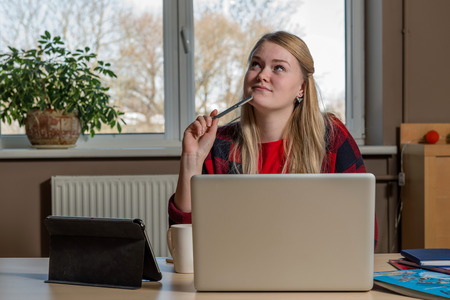 Smiling blonde woman sitting at a laptop drinking tea and working.の写真素材