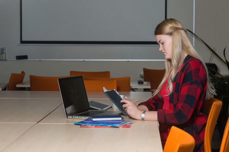 Smiling blonde woman sitting at a laptop drinking tea and working.の写真素材