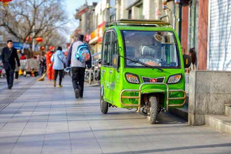 BEIJING, CHINA - MARCH 10, 2016:  People walk along the street. On the street is a parked scooter...