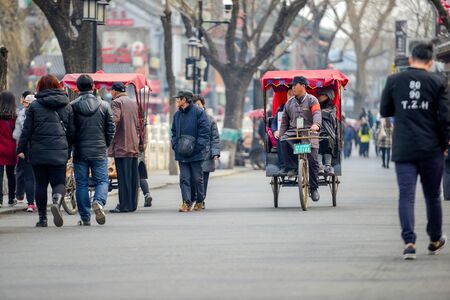 BEIJING, CHINA - MARCH 12, 2016: Tourists in a rickshaw in a hutong, Ancient hutongs are formed by...