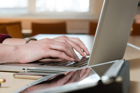 Woman sitting at a laptop and writing. There is a laptop, a tablet, a phone and a notebook on the table.の写真素材