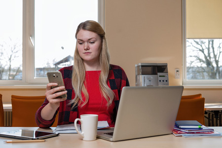 Smiling blonde woman sitting at a laptop drinking tea and working.の写真素材