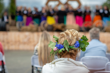 A woman with a flower crown in her head is watching a concert. View from the back.の写真素材