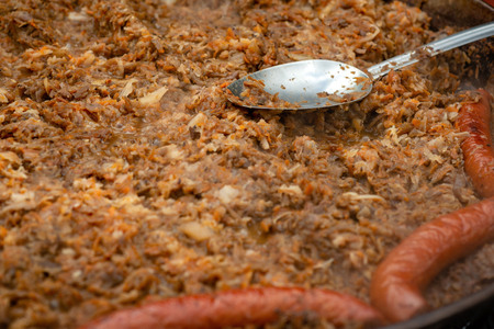 A spoon of metal in a pan with stewed cabbage and sausages.の写真素材
