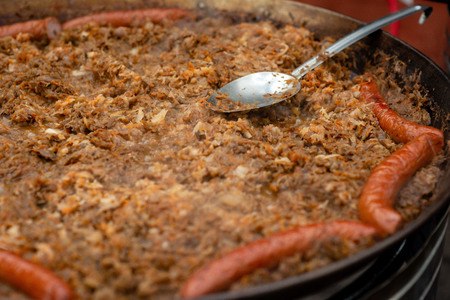 A spoon of metal in a pan with stewed cabbage and sausages.