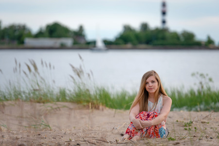 A young woman wearing a colorful long dress sitting on the beach.の写真素材
