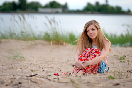 A young woman wearing a colorful long dress sitting on the beach.の写真素材