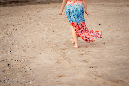 A young woman with bare feet and a colorful long gown walking along the beach. Only the lower part of the body is visible.の写真素材