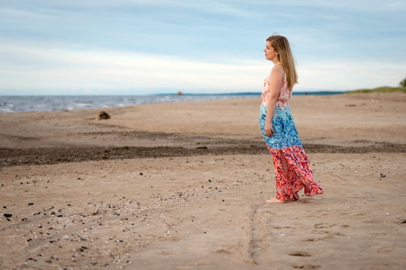 A young woman wearing a colorful long dress standing on the beach and looking at the sea.の写真素材