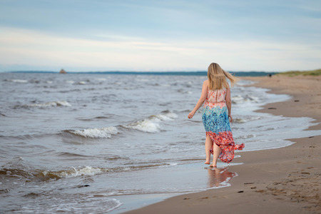 A young woman walking in the colorful long gown along the seafront.の写真素材