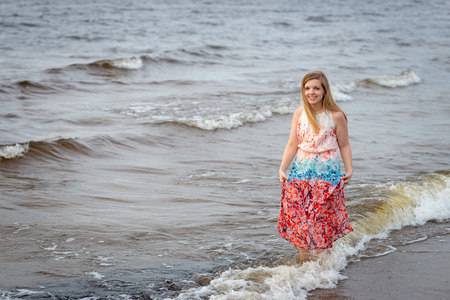 A smiling young woman walking in the colorful long gown along the seafront.の写真素材