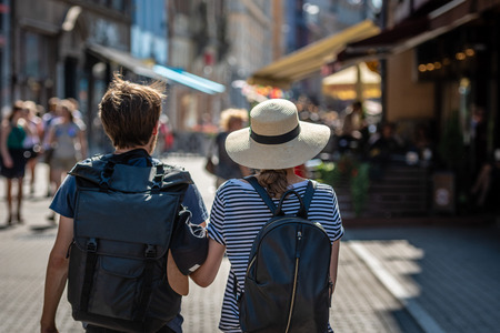 A couple of people with backpacks walking along the street. View from the back.の写真素材