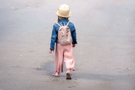 A little girl with a backpack going along the sidewalk. View from the back.の写真素材