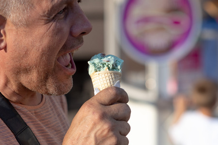 A middle age man eating ice cream on the street.の写真素材
