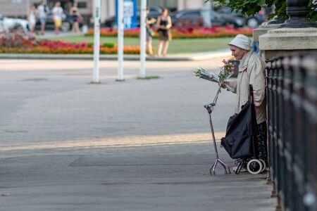 RIGA, LATVIA - JULY 26, 2018: An old woman standing at the bridge railing and selling flowers.のeditorial素材